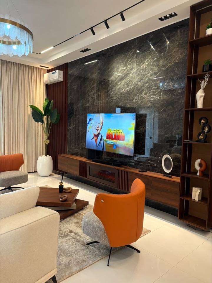 Living room by CK with a dark marble media wall, walnut joinery, track lighting and orange lounge chairs