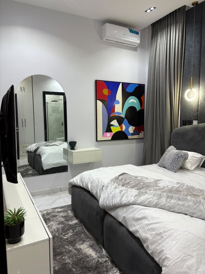 Guest bedroom with layered white bedding, statement artwork and a wall-mounted TV